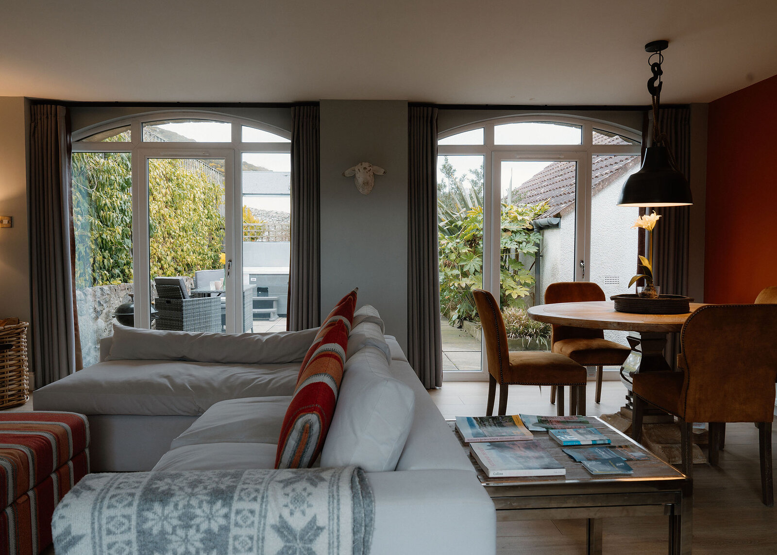 Two arched glazed doors look out on a courtyard with a hot tub and a planted garden, past a white sofa and dining table.