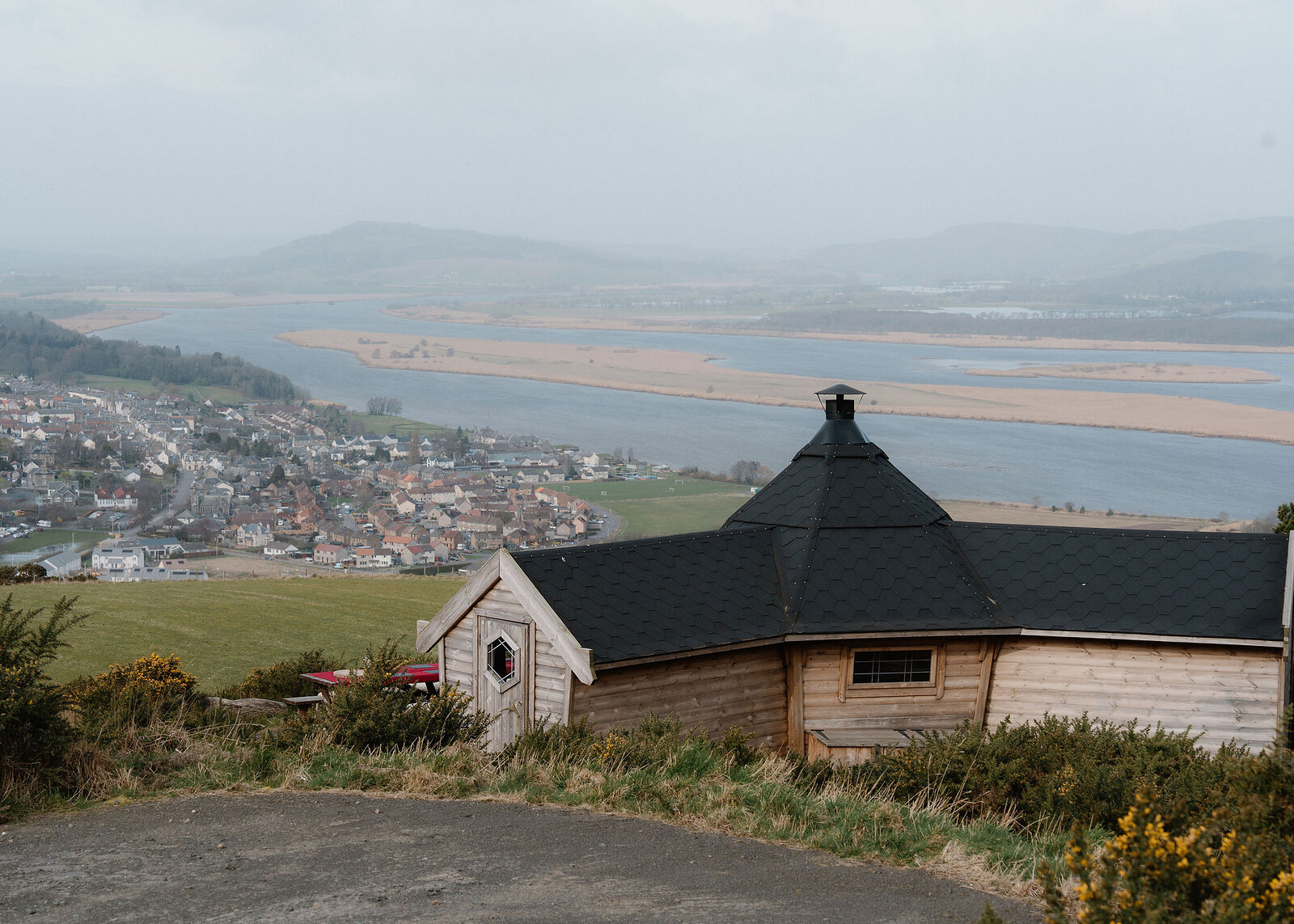 The Hide seen closer from the gravel turning circle, its gable door and black roof filling the lower half above Newburgh and the River Tay.