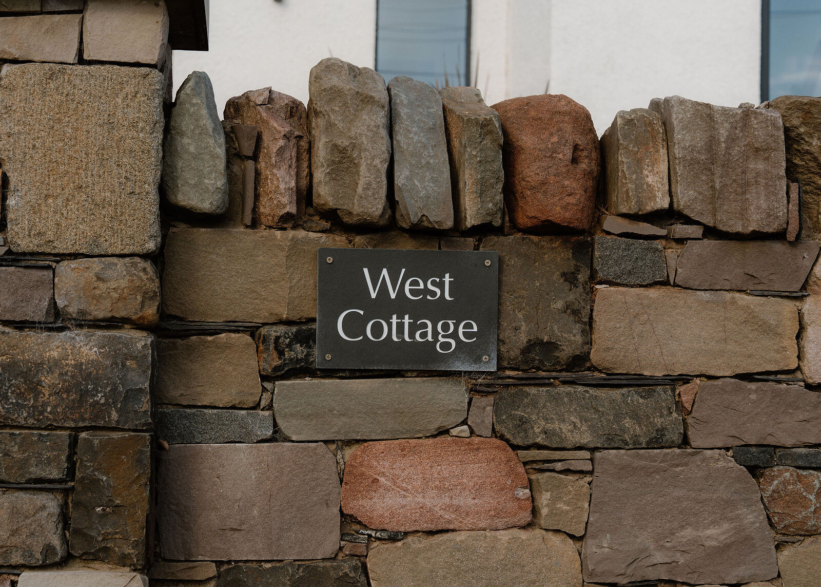 A stone wall carries an engraved sign reading "West Cottage".