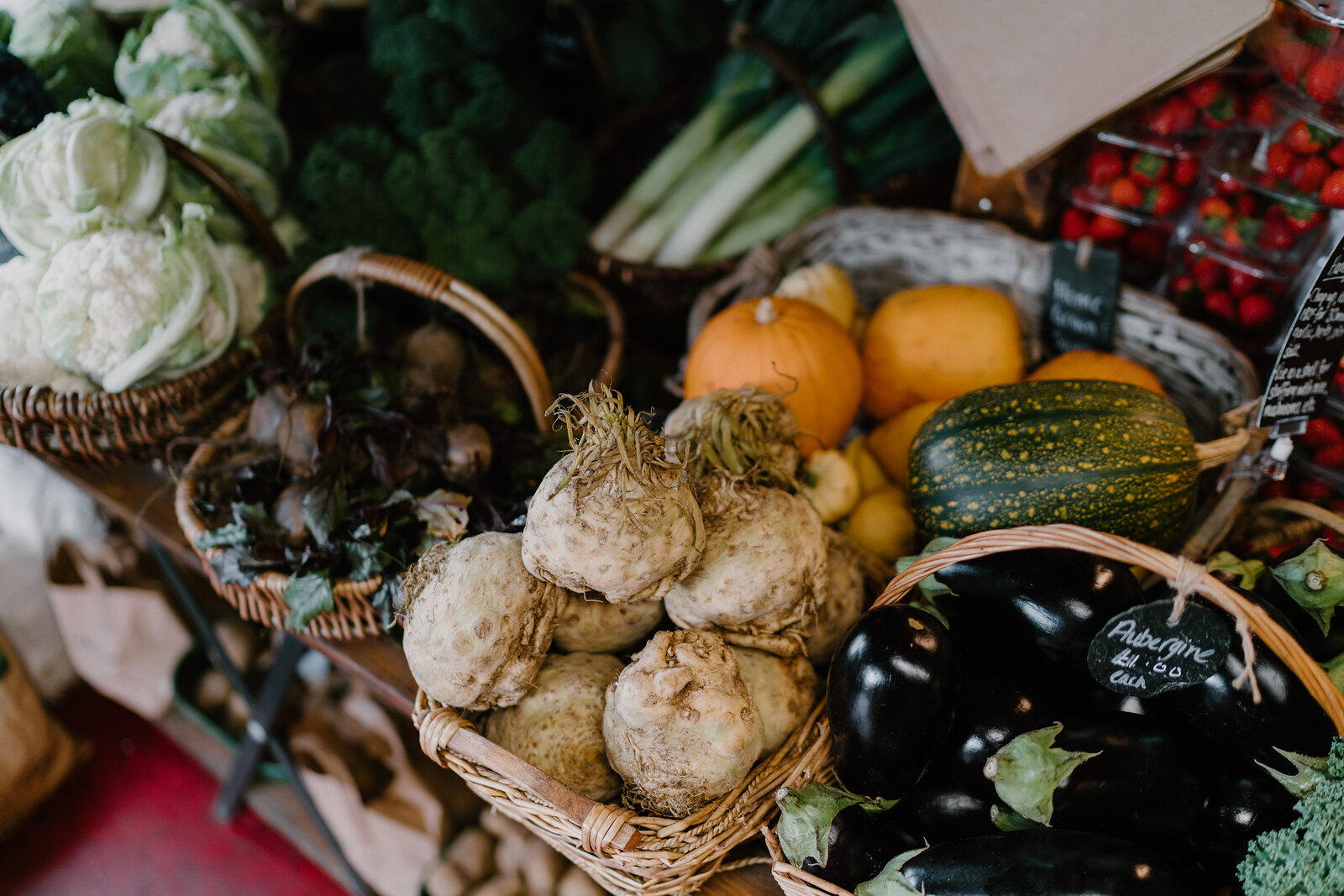 Wicker baskets hold cauliflowers, celeriac, squash, tomatoes and aubergines on a market stall.