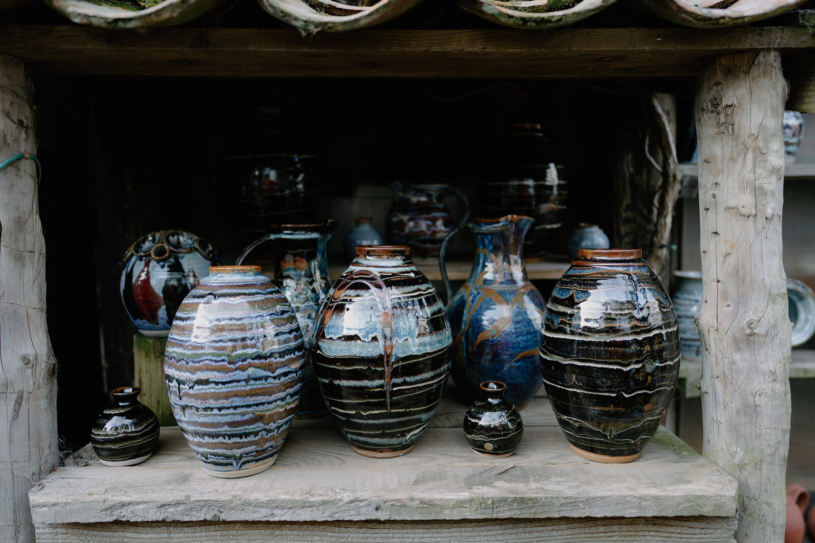 Glazed ceramic jugs and vases in swirling blue and brown patterns stand on a wooden shelf.