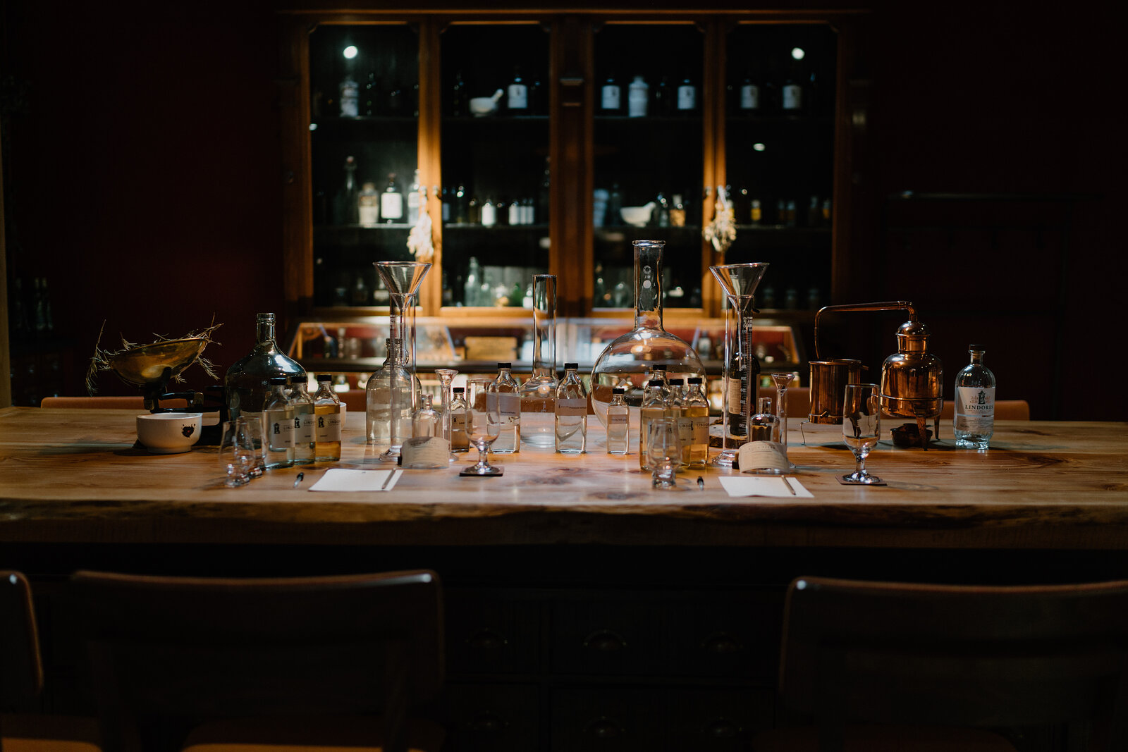 A dark wood-panelled bar holds rows of glasses, spirit bottles and a hanging rack of stemware lit against a stone wall.