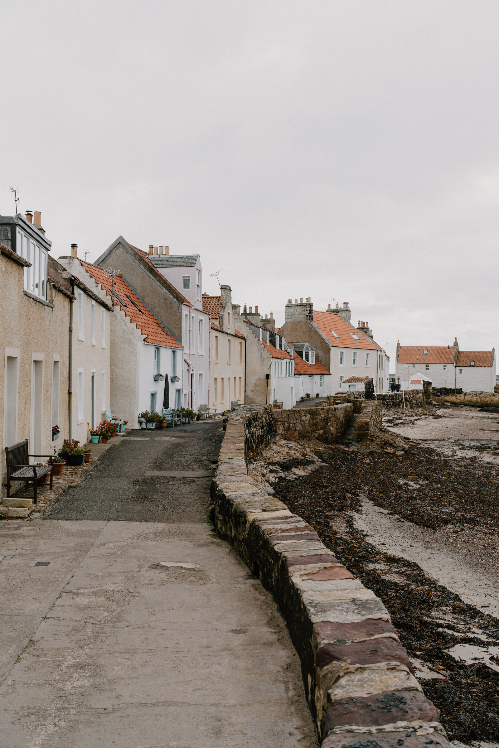 Whitewashed and pastel cottages with red pantiled roofs line a harbour path, a stone sea wall running along the shore.