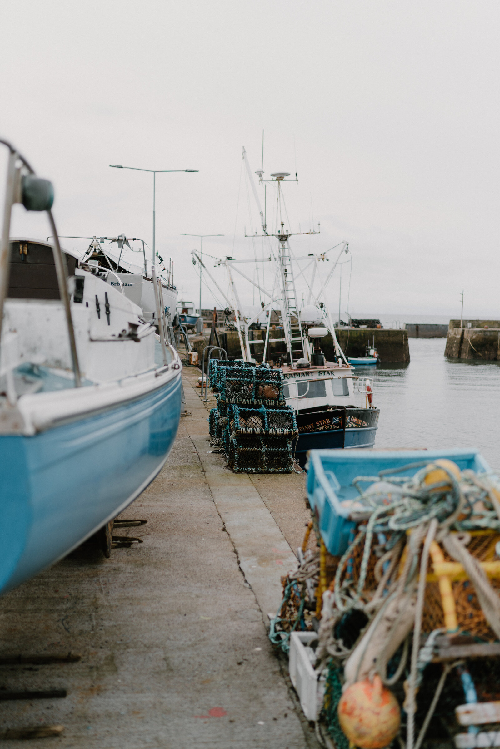 Fishing boats named "Radiant Star" are moored at a harbour quay, lobster creels and coiled rope piled on the pier beside them.