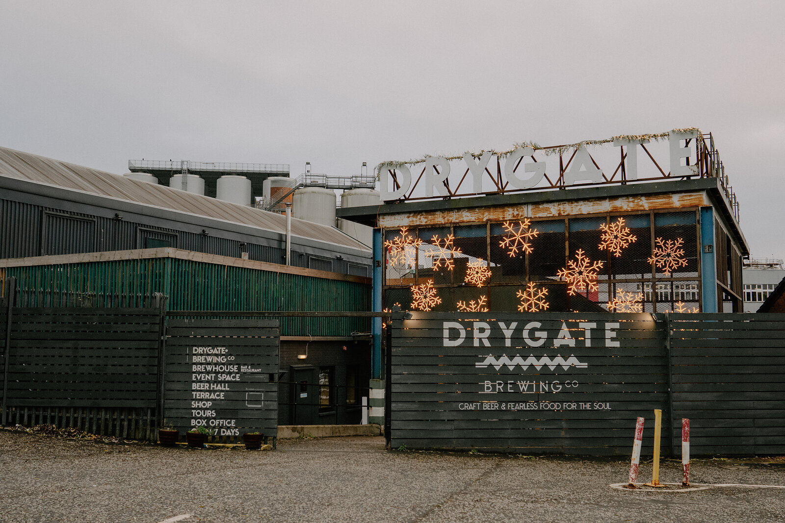 A mural reading "DRYGATE BREWING — Craft beer & flavours food for the soul" covers the side of an industrial building, snowflake lights strung along the roofline.