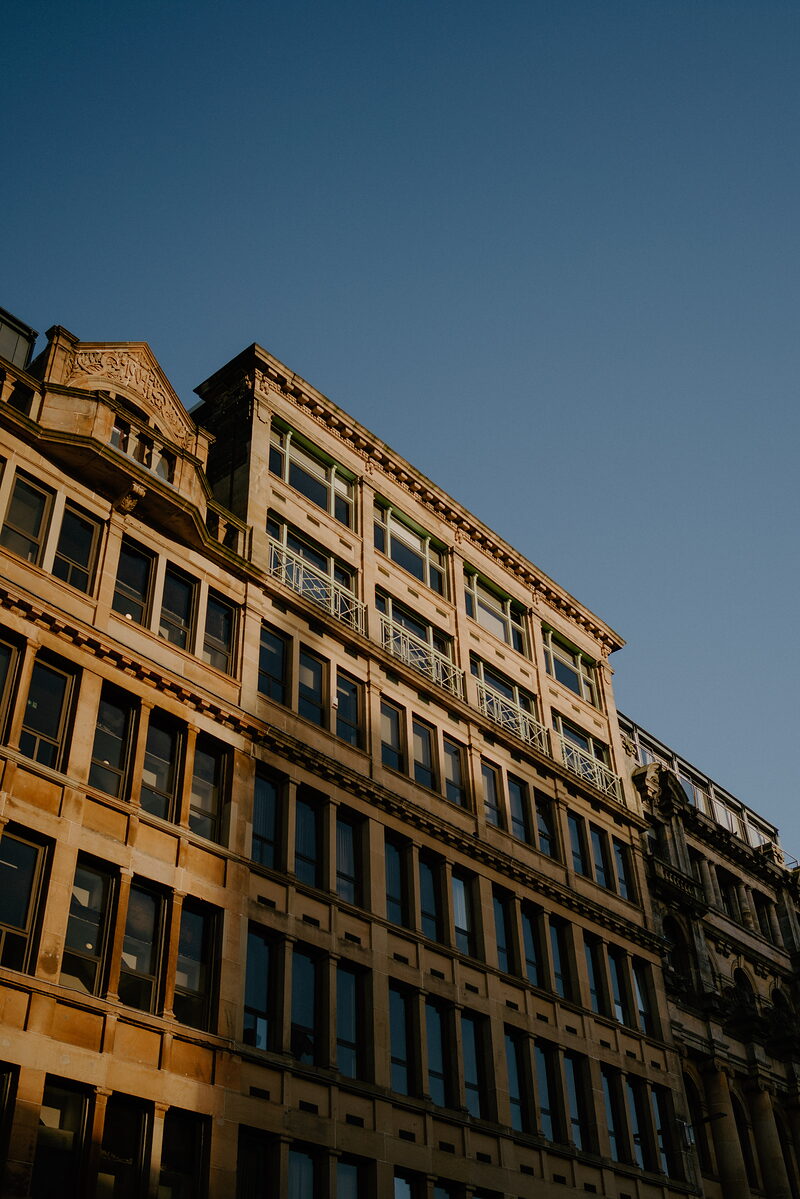 A sandstone office building's ornate upper storeys catch low evening sun against a deep blue sky.