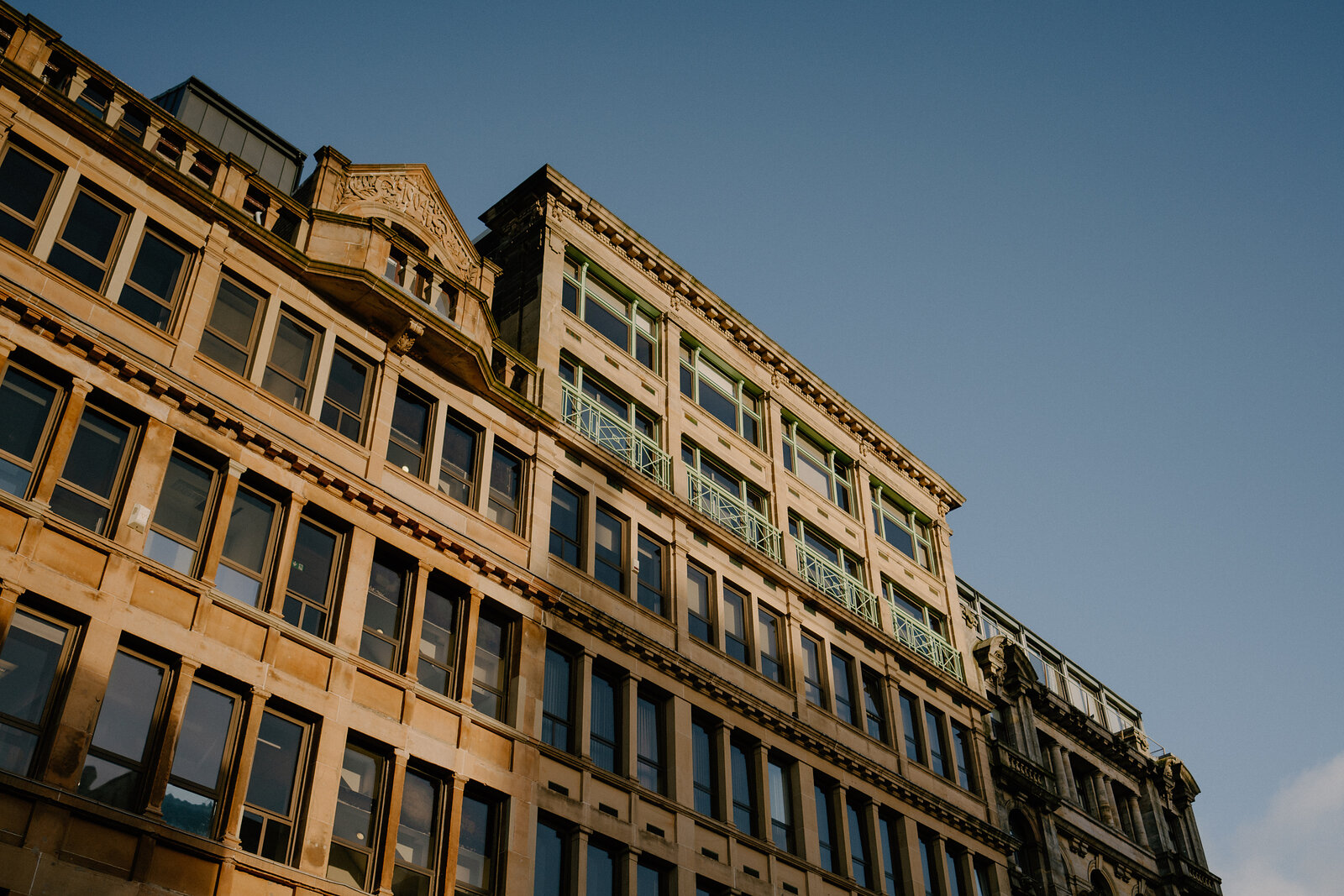 A sandstone office building's ornate cornicing and tiered windows catch evening light against a deep blue sky.
