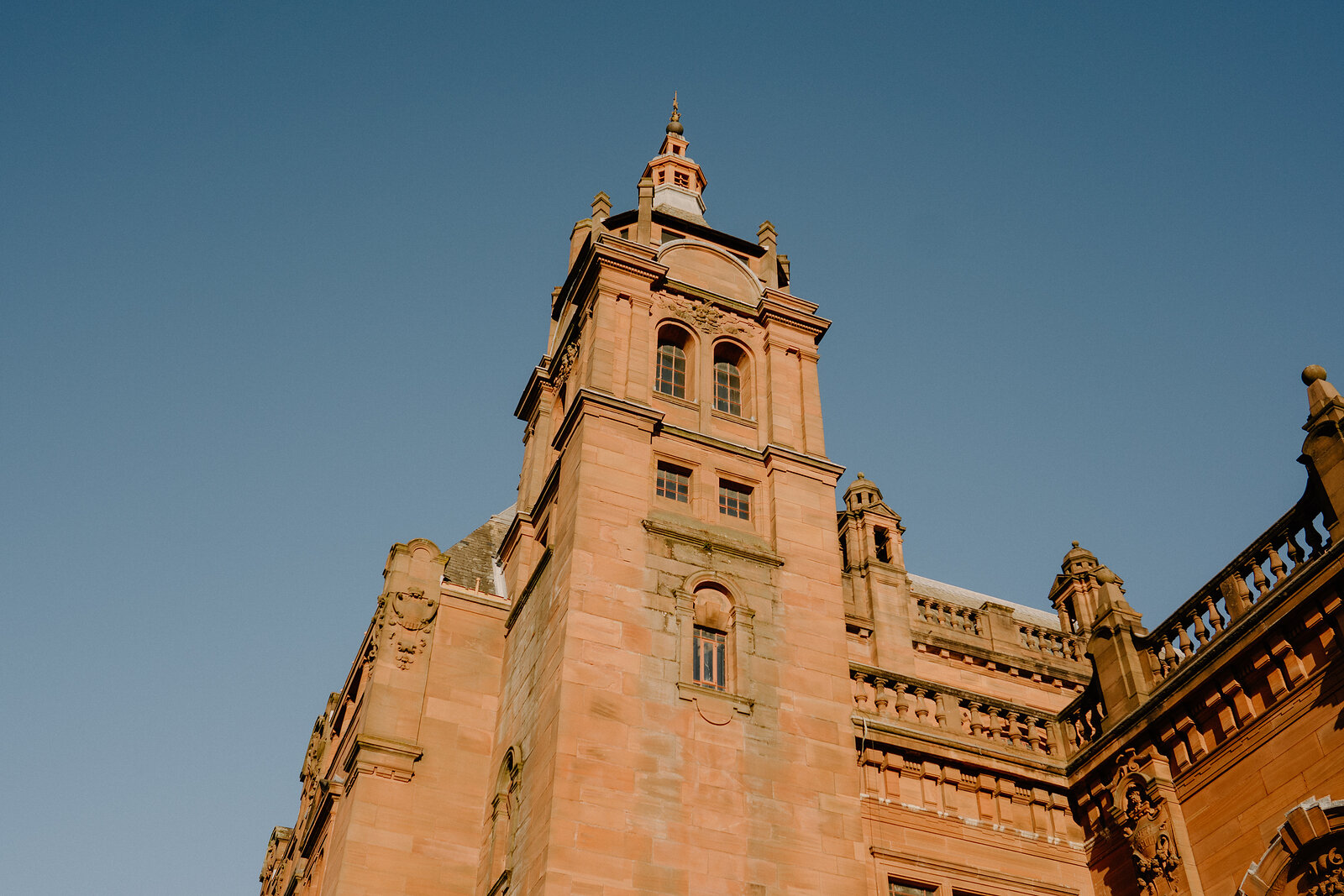 A sandstone clock tower with a domed cupola and pilastered facade rises against a clear blue sky.
