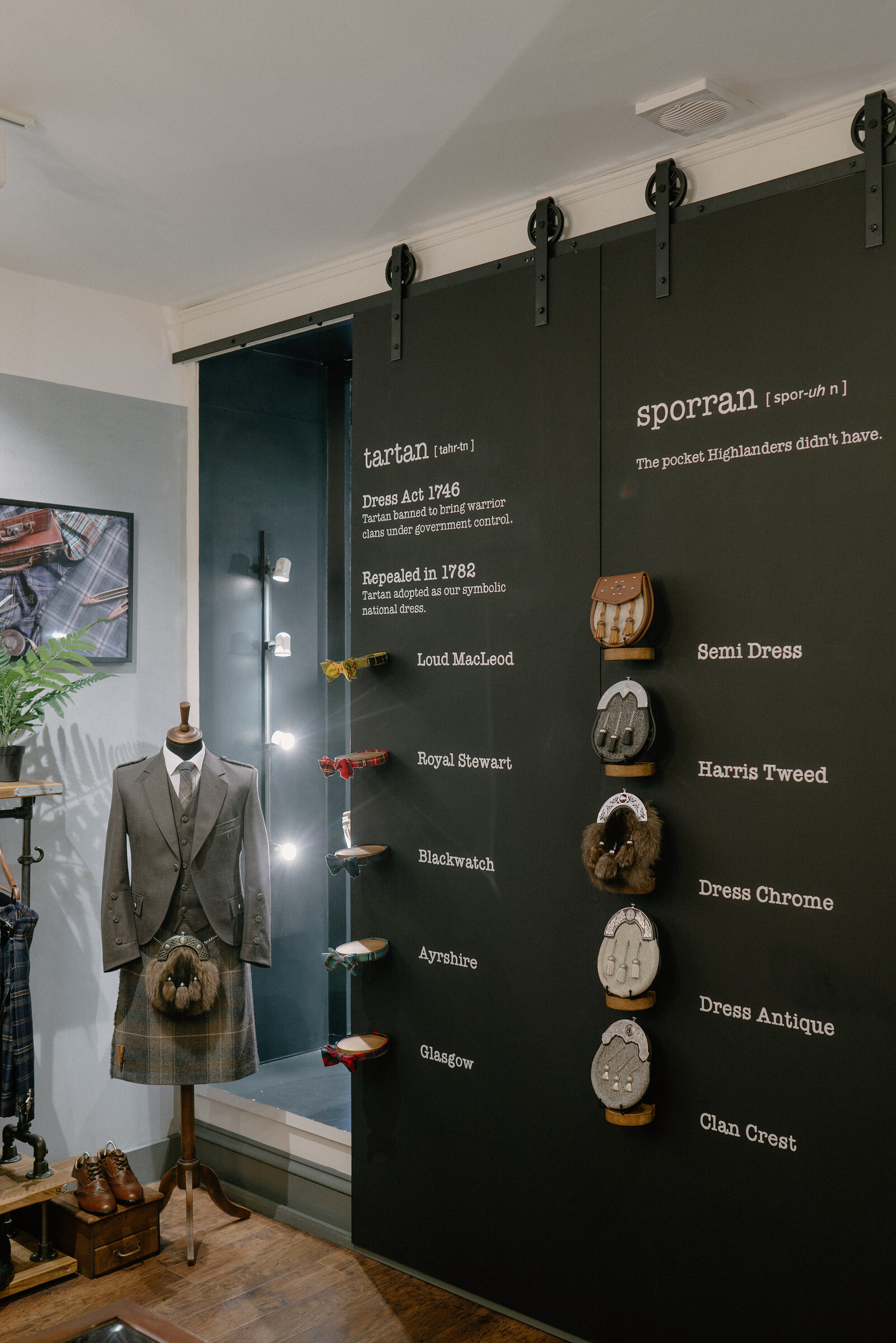 A shop display explains tartan and sporran history on a black wall, a mannequin dressed in a kilt outfit standing beside hanging sporrans.