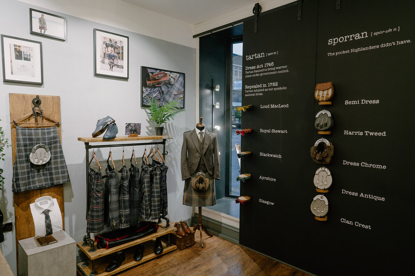A shop display explains tartan and sporran history on a black wall, framed photographs and a mannequin dressed in a kilt outfit with hanging kilts on a rail.