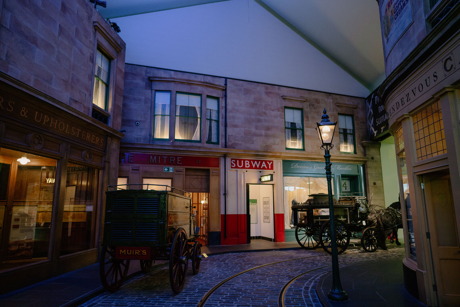 A museum exhibit recreates a Victorian street with a horse-drawn cart, gas lamp and a shopfront reading 'Subway' beneath a glazed roof.