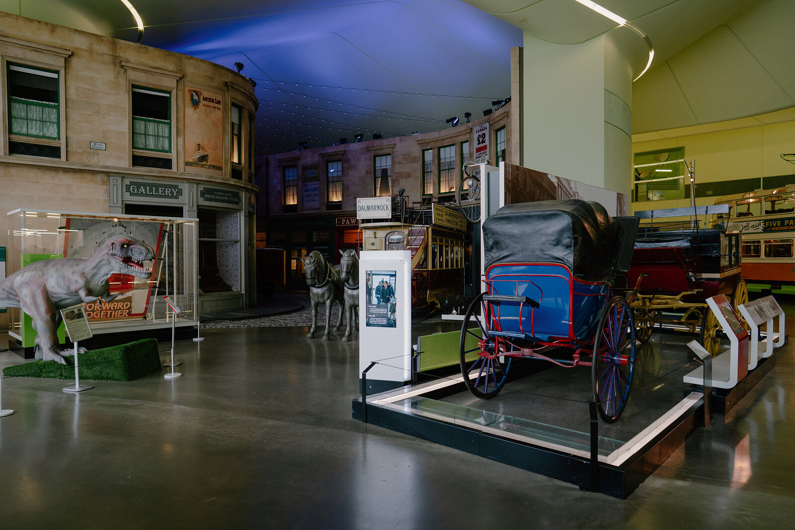 A museum exhibit recreates a Victorian street with shopfronts and a horse-drawn carriage, a taxidermy horse and dinosaur model visible in glass cases nearby.