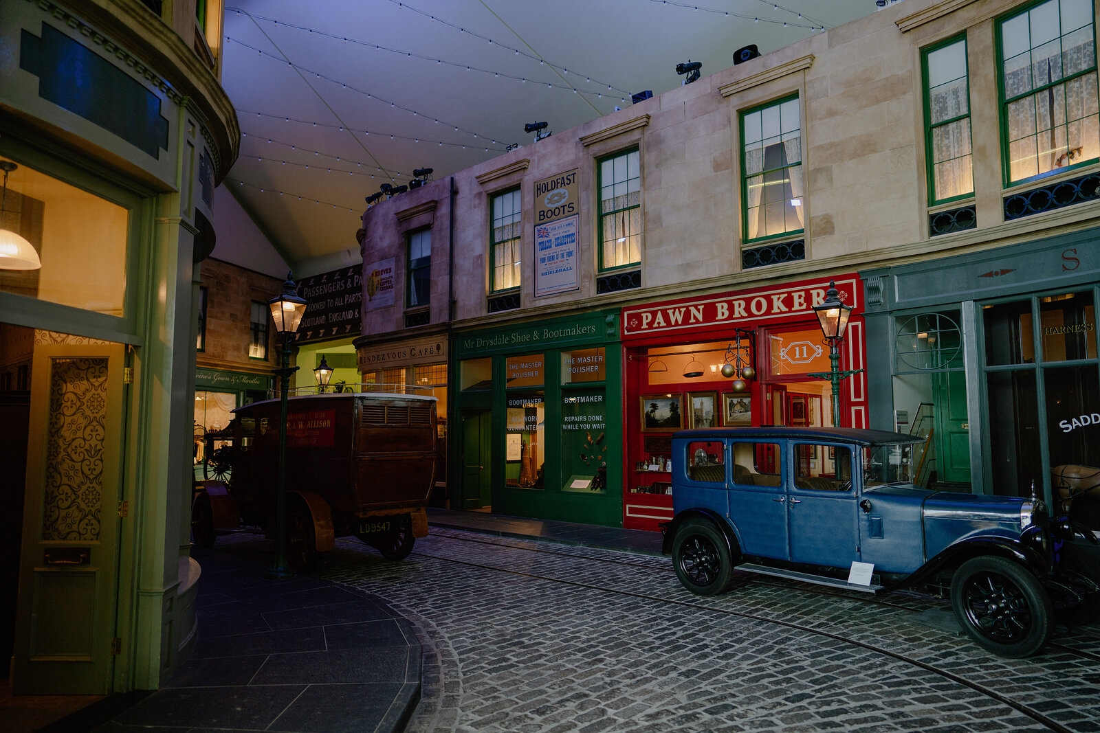 A museum exhibit recreates a Victorian street with a shopfront reading 'Pawn Broker' beside a vintage blue car and a horse-drawn cart.
