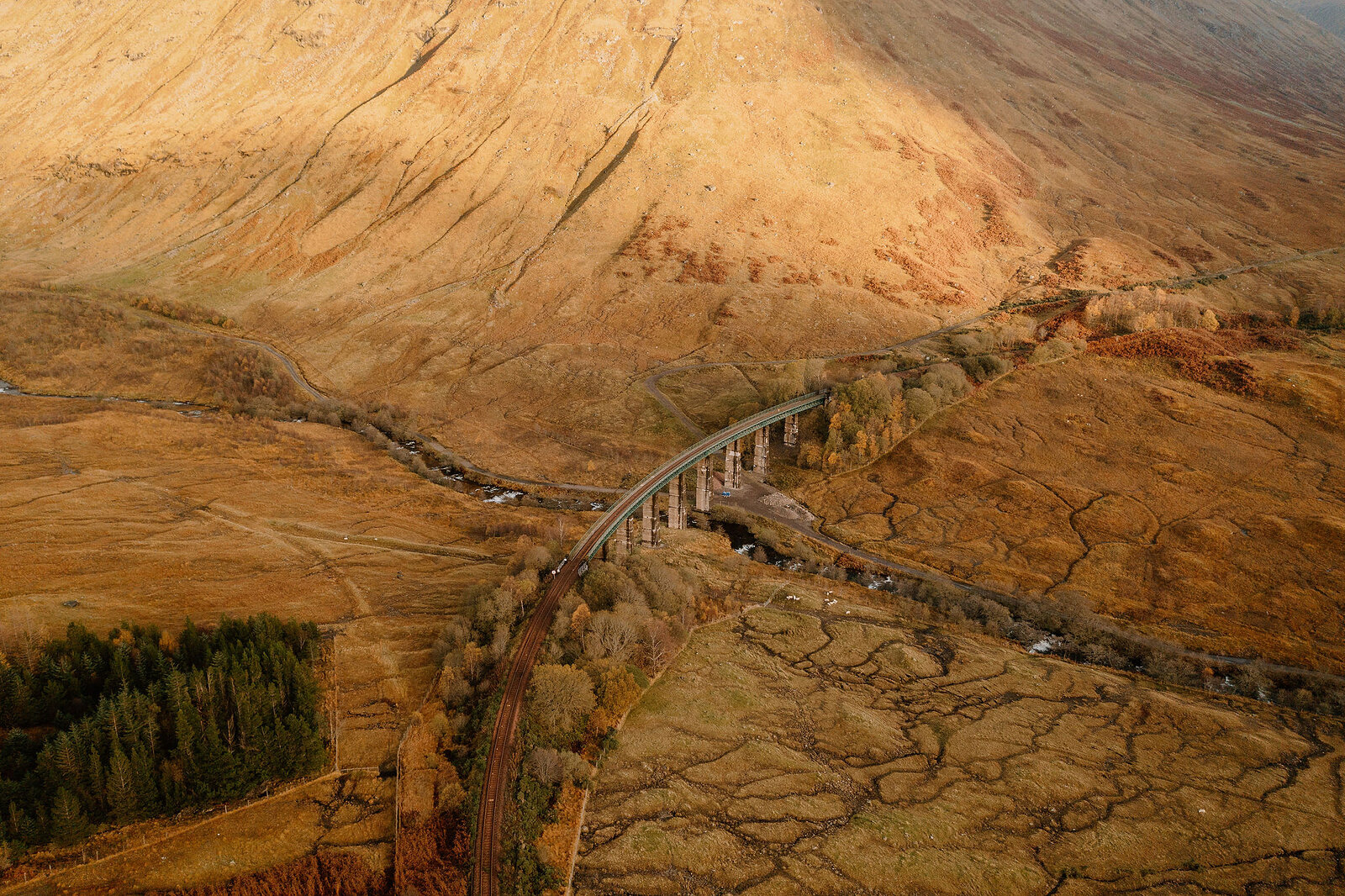 A curved railway viaduct crosses a river at the foot of an autumn-coloured glen, mountains rising sharply on either side.