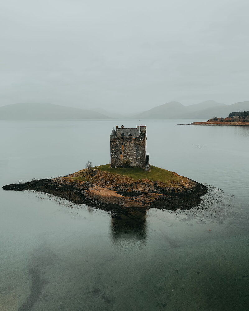 Castle Stalker on its islet in still, grey water.
