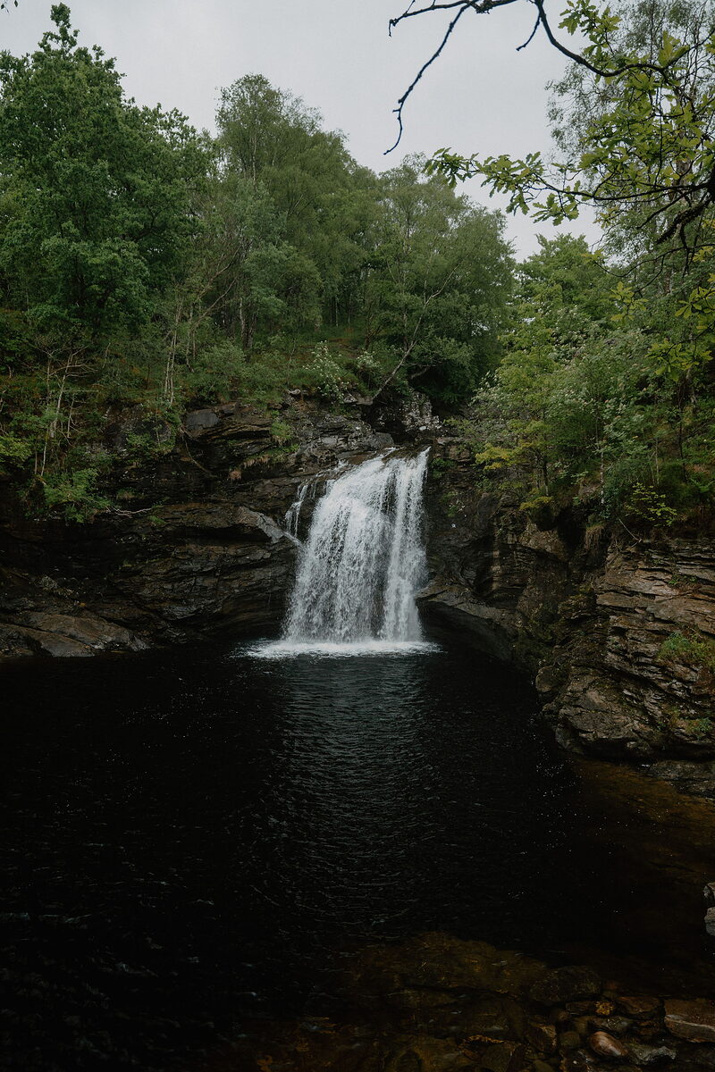 The Falls of Falloch dropping into a dark pool among green woods.