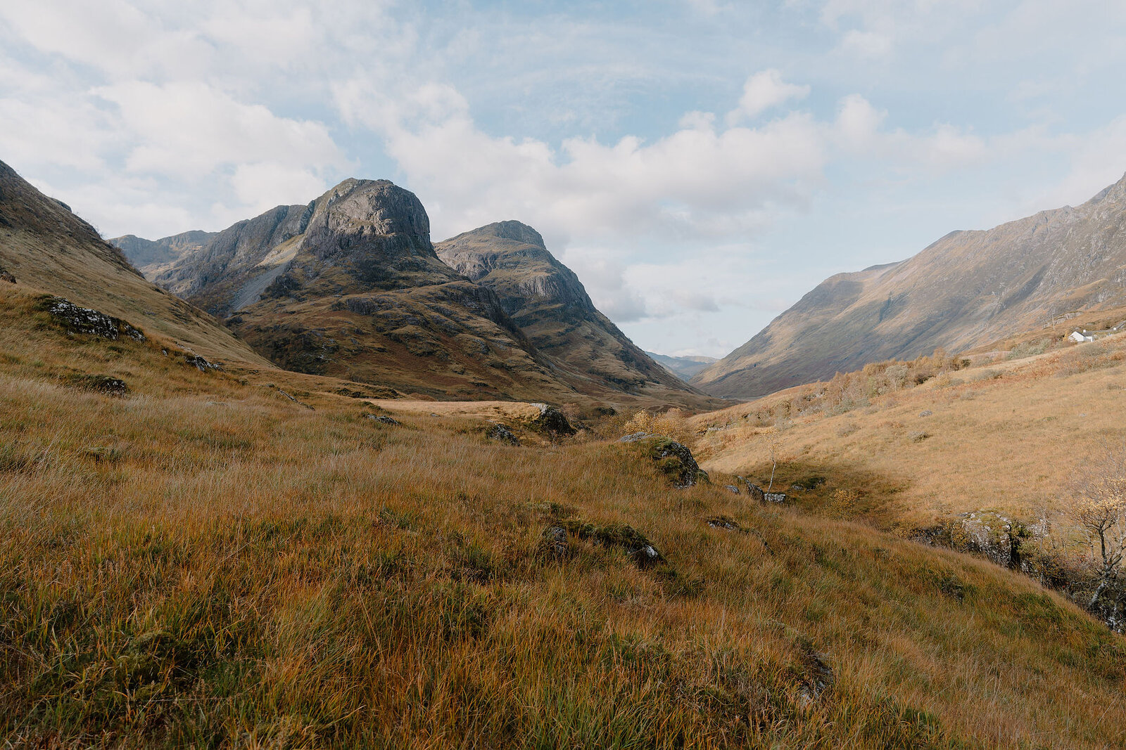 Two rugged mountain peaks rise above a golden autumn glen, moorland stretching between them.