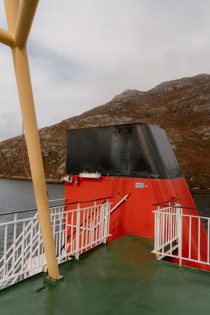 The stern of a ferry with its black-tipped funnel, hills rising beyond the water.