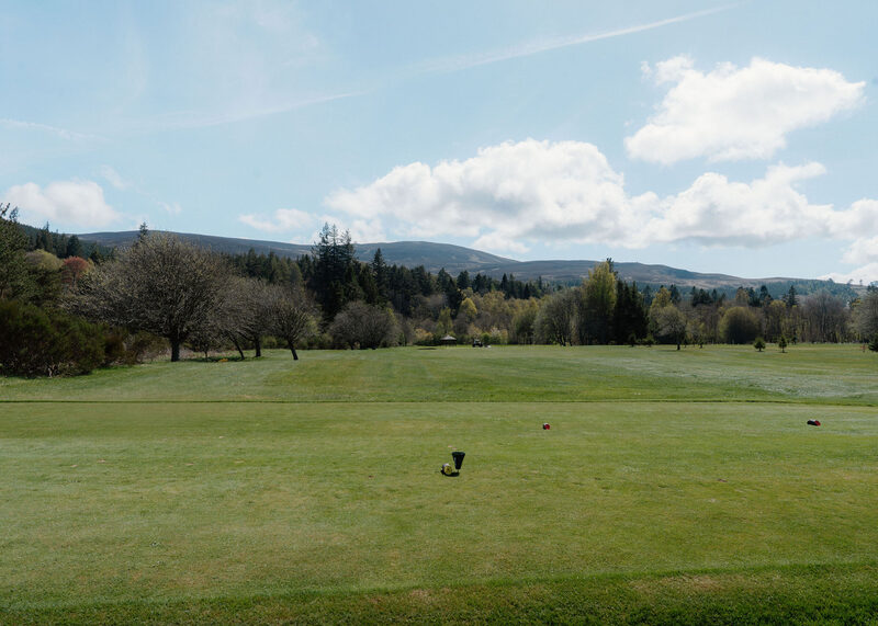 A tee box and fairway with woods and hills on the horizon.