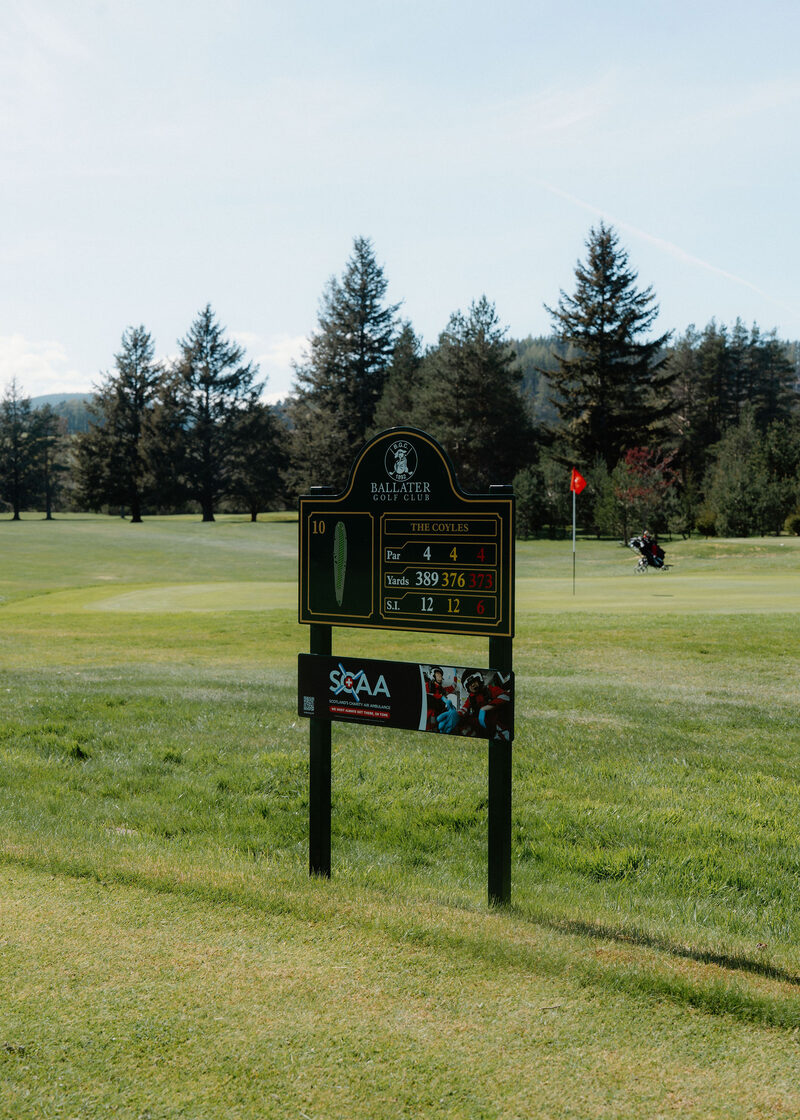 The 10th tee sign at Ballater Golf Club, The Coyles, par 4, 389 yards, with a green and pines behind.
