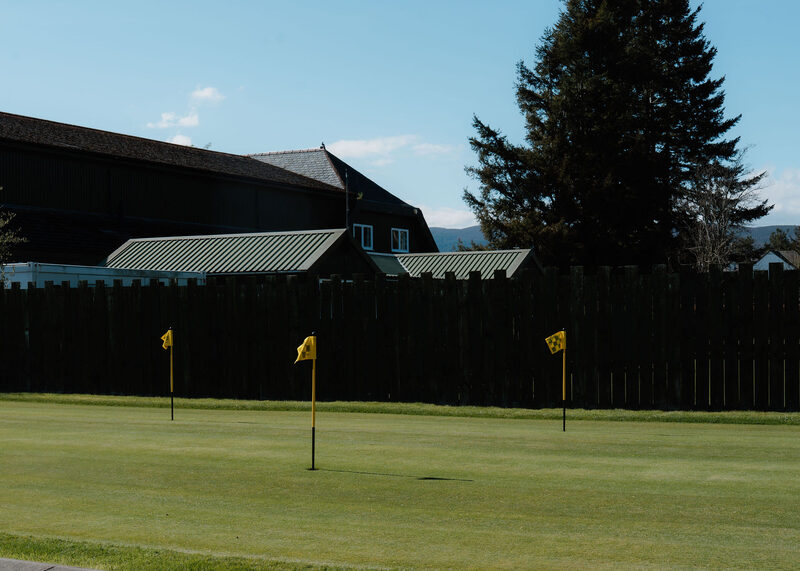 A putting green with three yellow flags beside the clubhouse.