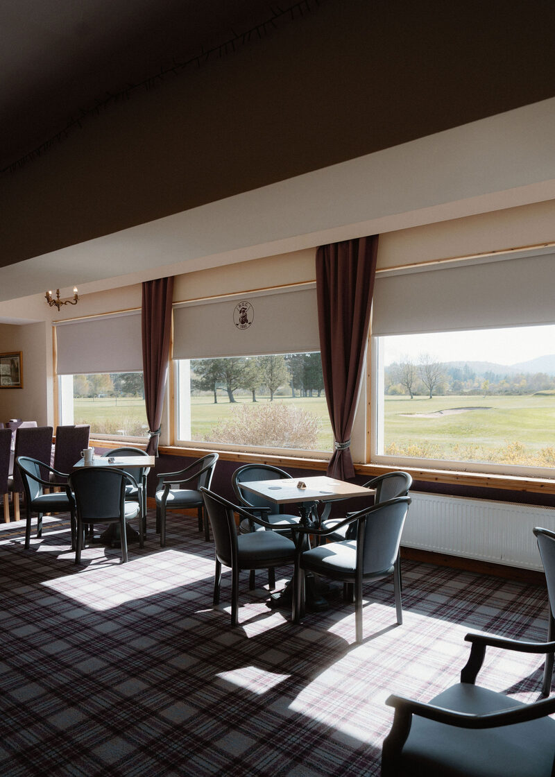 Tables and chairs in the clubhouse restaurant, with big windows over the course.