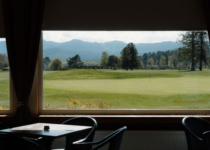 The view from the clubhouse restaurant window over a green to pines and hills.