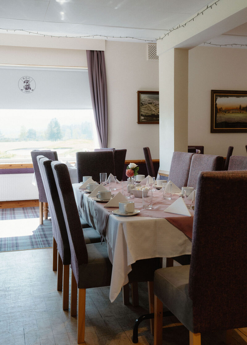 A long table laid for a meal in a clubhouse dining room with pictures on the walls.