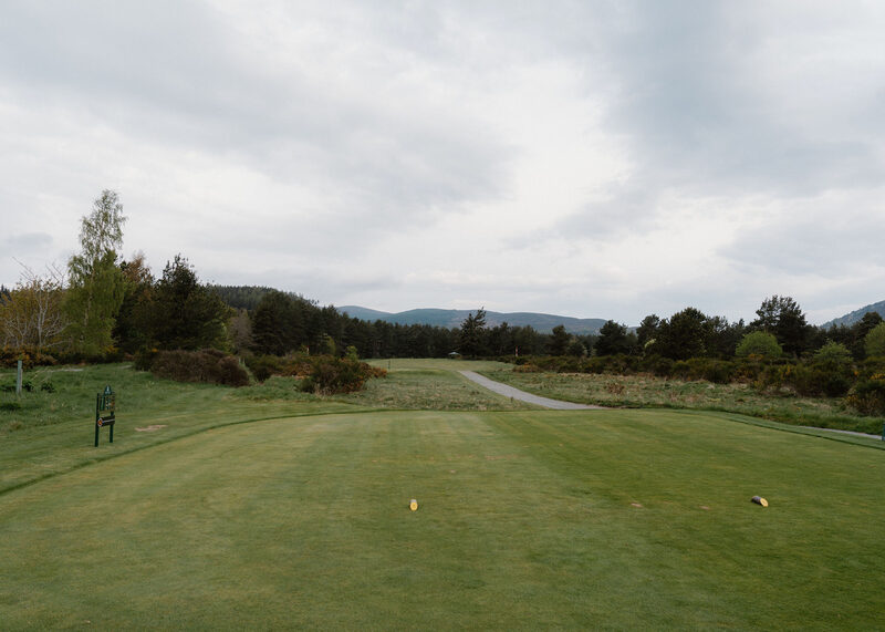 A tee with yellow markers looking down a fairway past a hole sign and gorse.