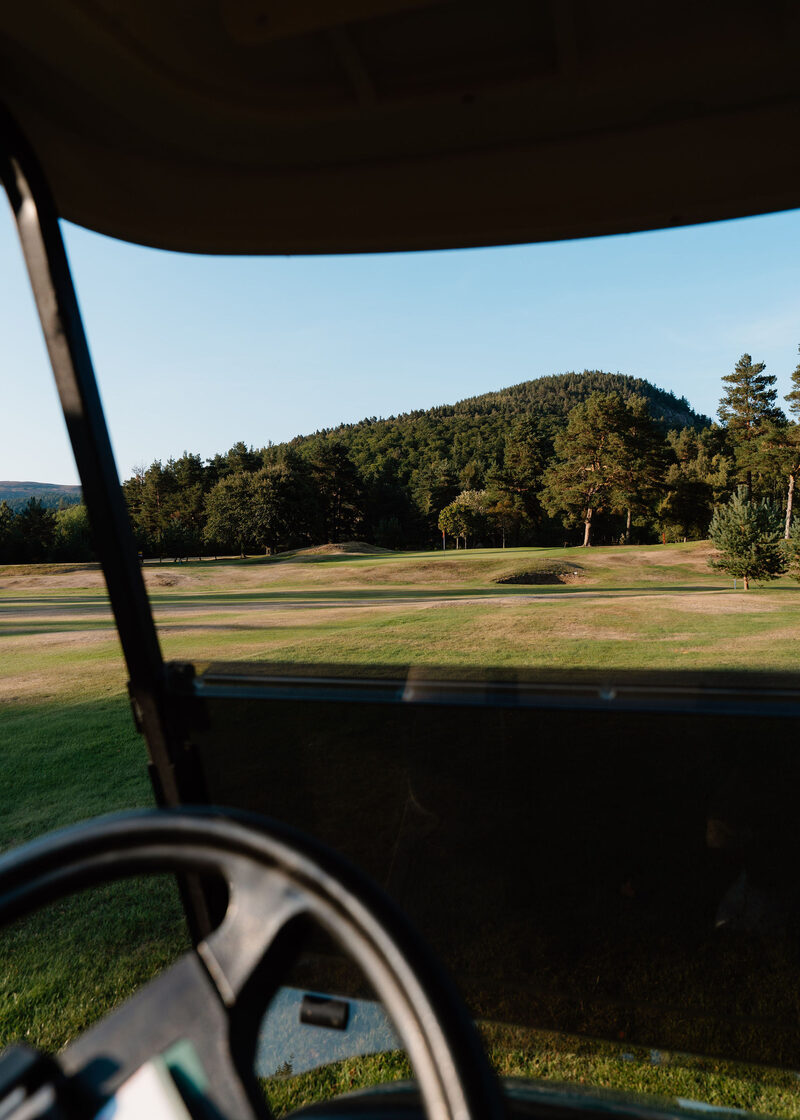 A rounded wooded hill seen over the fairway from a buggy.