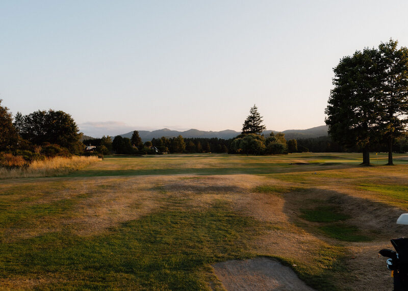 A dry late summer fairway with hollows and a bunker, and hills on the horizon.