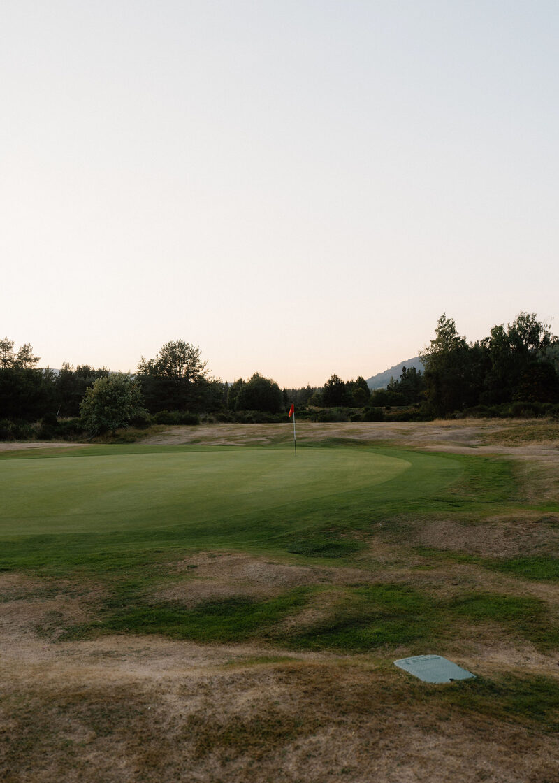 A green with a red flag at dusk, with low hills beyond.