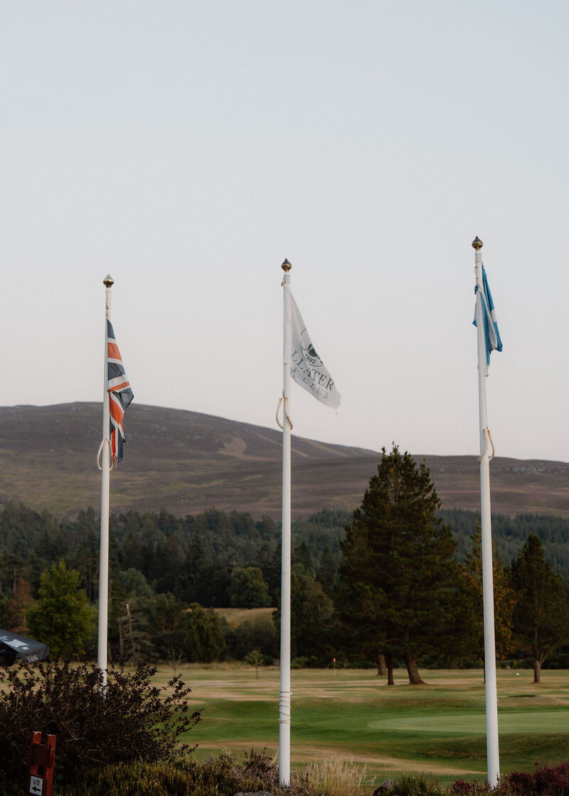 The Union flag, the club flag and the saltire on flagpoles, with a heather hill behind.