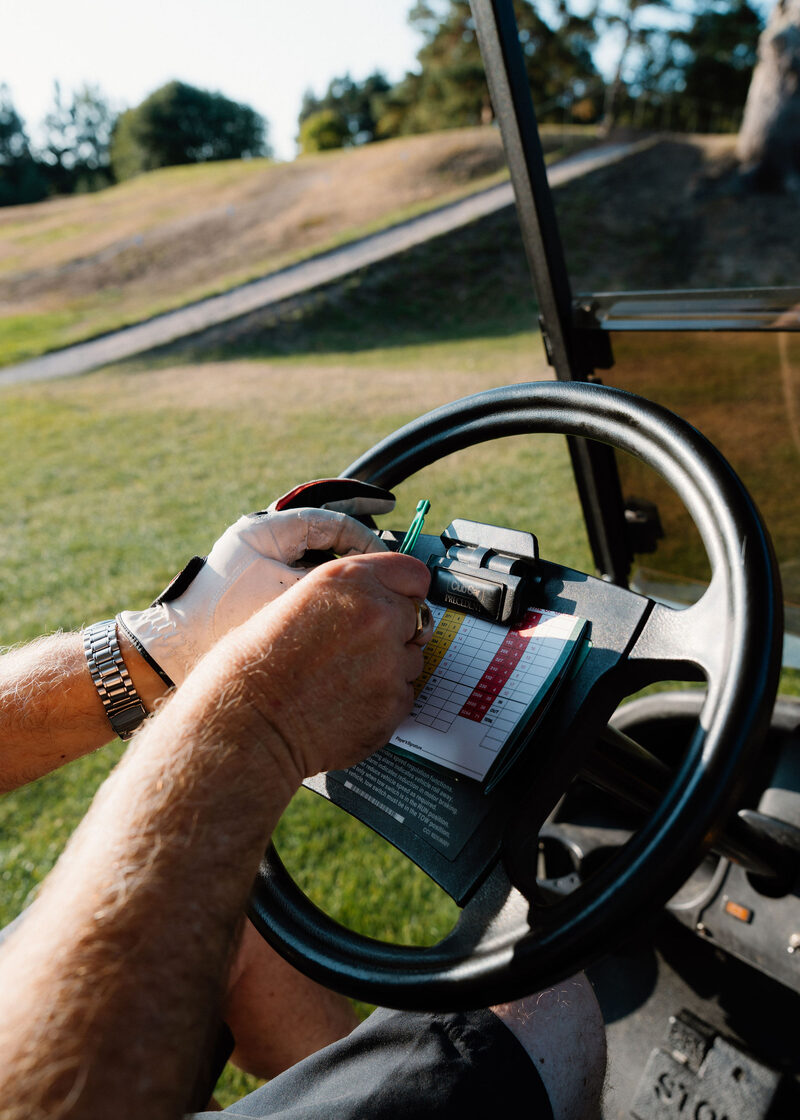 Gloved hands marking a scorecard clipped to a buggy’s steering wheel.