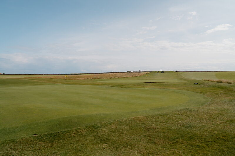 A putting green rolling towards the horizon on a coastal links course