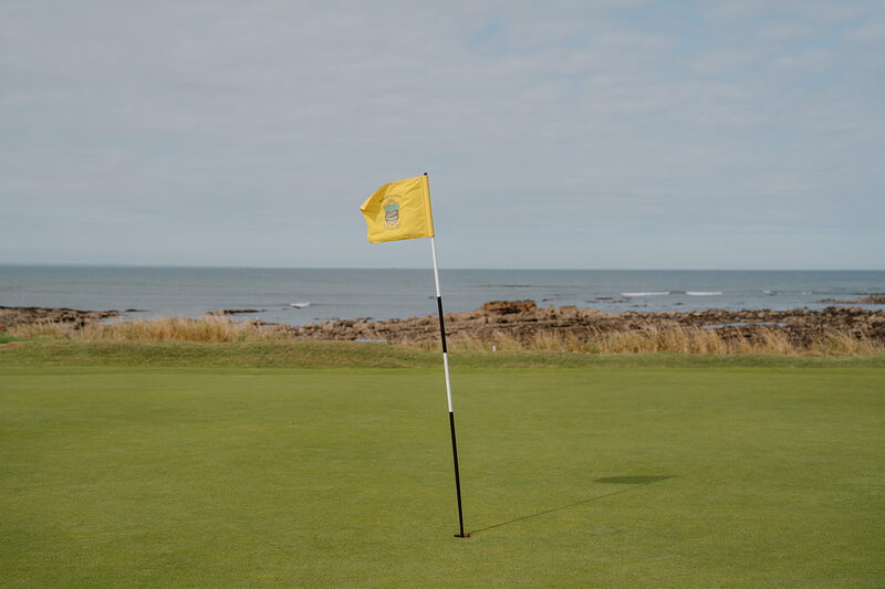 A yellow flag fluttering beside a green overlooking rocky coastline and the sea