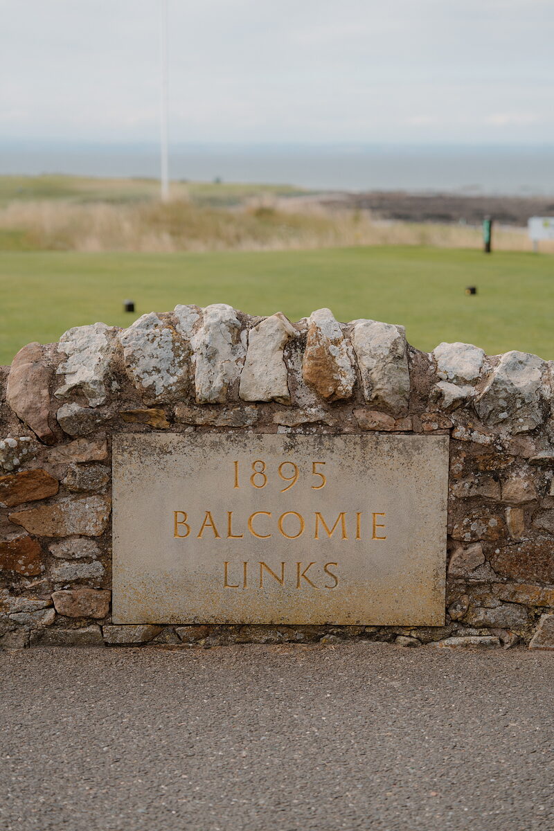 A stone plaque reading 1895 Balcomie Links set into a dry-stone wall overlooking the fairway and sea