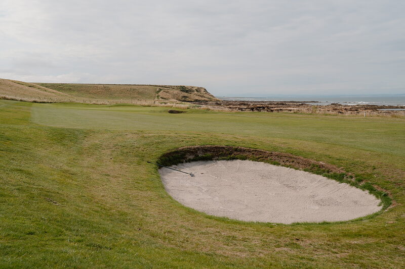 A deep bunker beside a green overlooking rocky cliffs and the sea