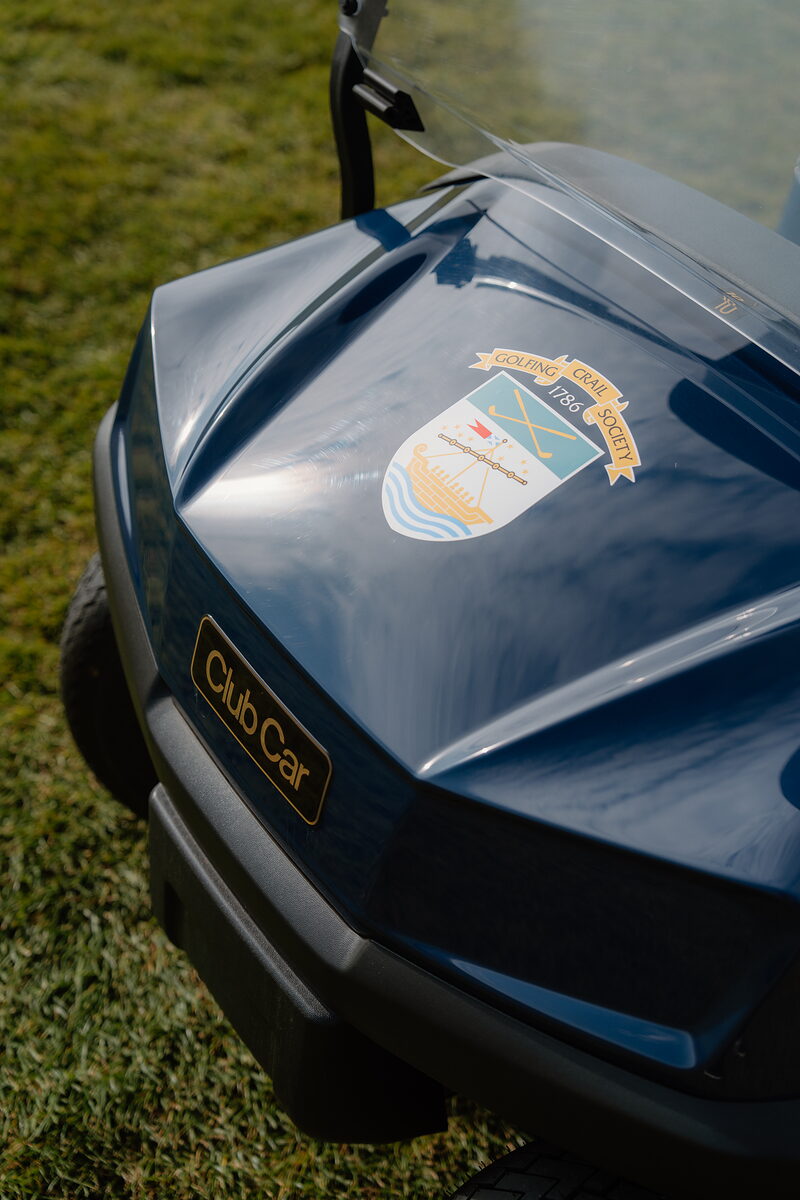 The Crail Golfing Society crest on the hood of a blue golf buggy, parked on the grass