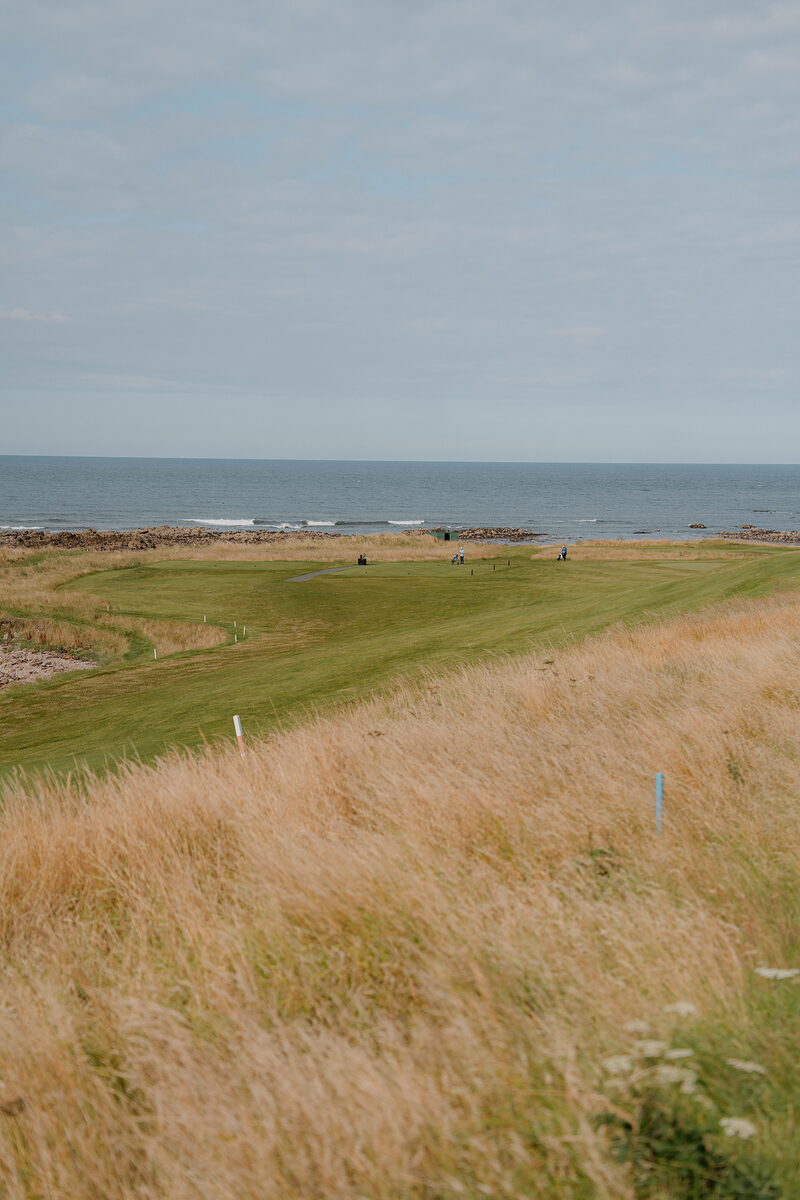 Golfers on a fairway bordered by rocky coastline and the sea