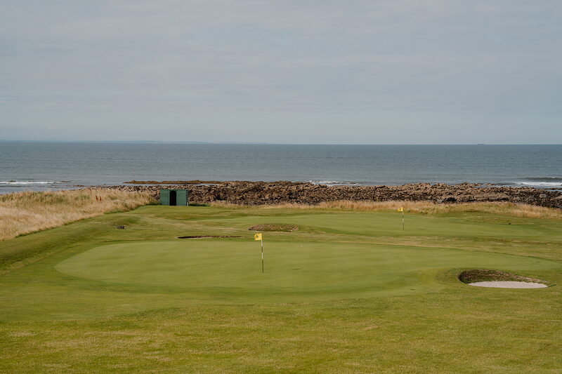 A green beside the sea, its flag marking the hole and a rocky shoreline running behind