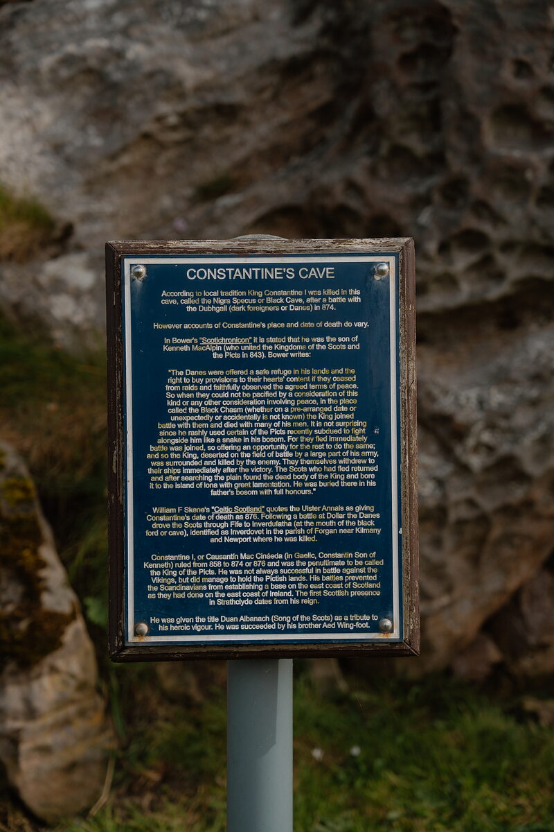 An information board reading Constantine's Cave mounted before a rocky outcrop