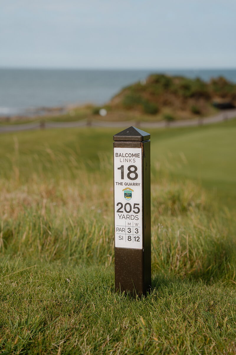 A marker post reading Balcomie Links, hole 18, The Quarry, 205 yards, standing above the sea