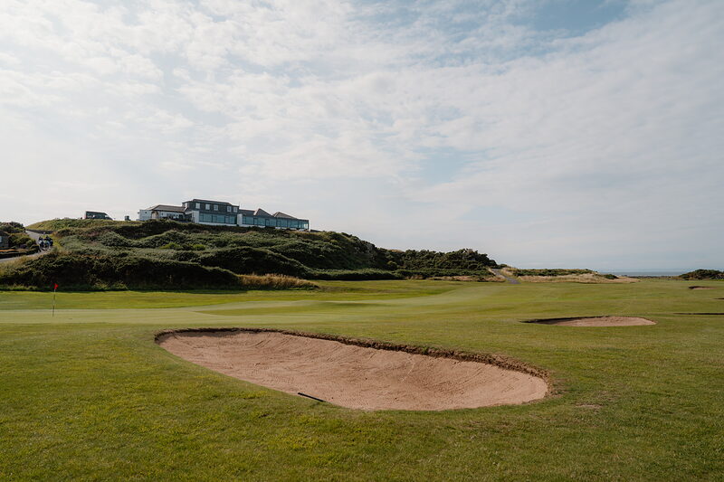Twin bunkers before a green, a blue clubhouse perched on a rise above the dunes