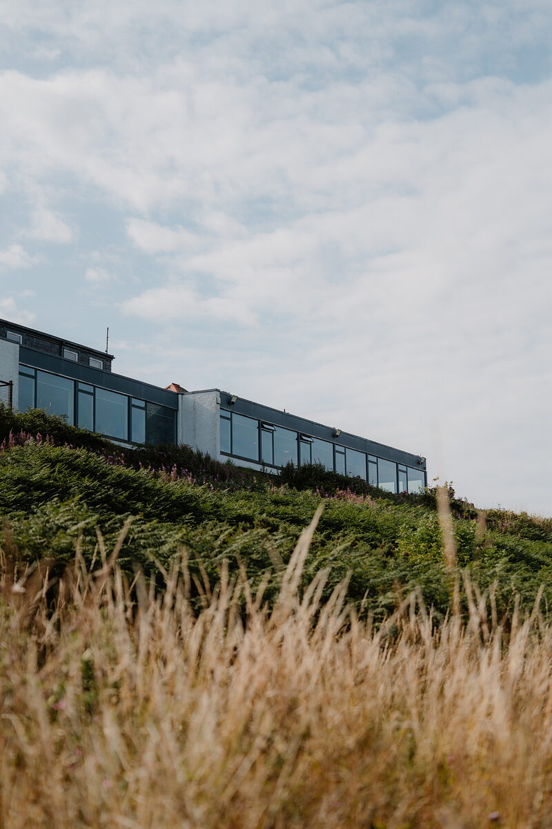 The modern glass clubhouse at Crail Golfing Society, seen from a bank of grass on the hillside
