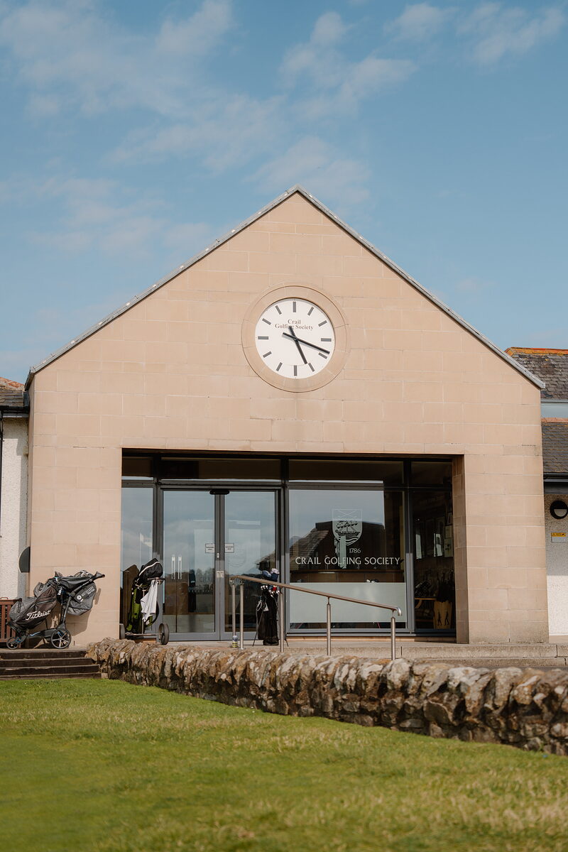 The clock-faced gable end of the Crail Golfing Society clubhouse, with golf trolleys parked by the entrance