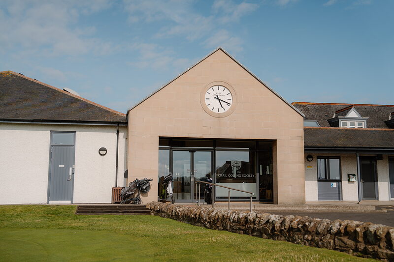 The clock-faced gable of the Crail Golfing Society clubhouse, with golf trolleys parked at the entrance