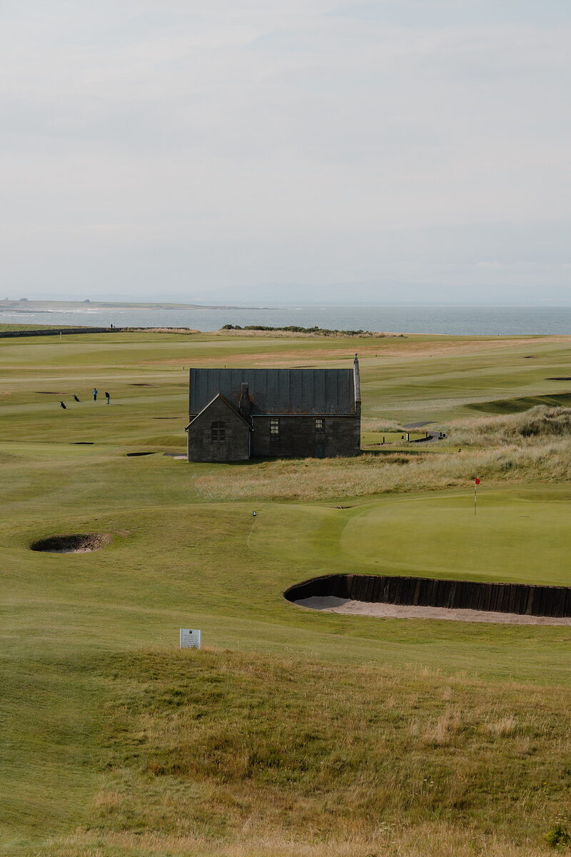 A stone cottage beside the green at Crail, bunkers either side and the sea beyond