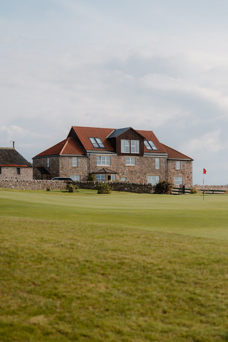 A stone clubhouse with a red-tiled roof standing beyond the green at Crail, a flag marking the hole
