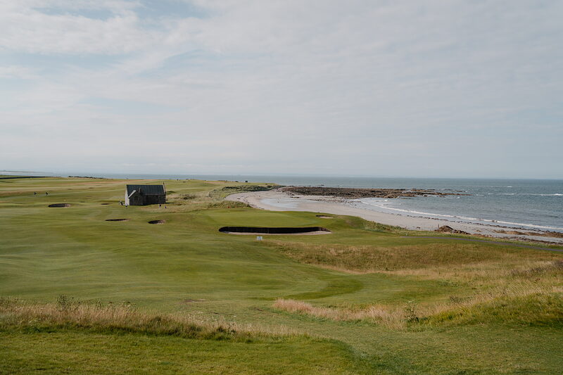 A stone shelter and bunkers beside the green at Crail, a stony shoreline stretching along the coast